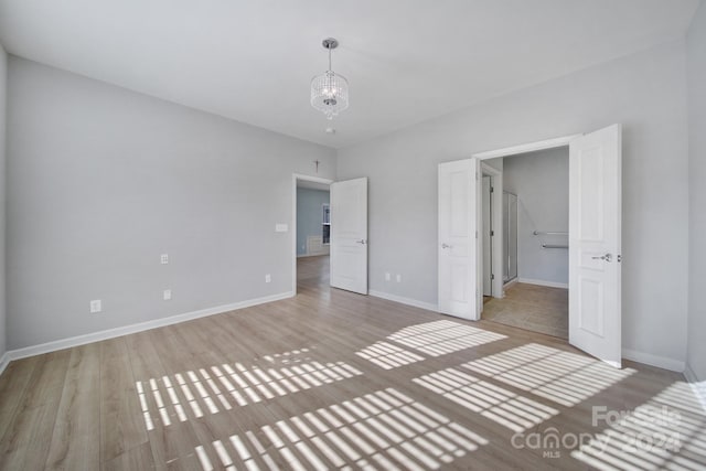 unfurnished bedroom featuring a notable chandelier and light hardwood / wood-style flooring