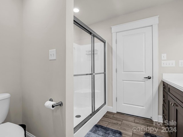 bathroom with toilet, vanity, a shower with shower door, and hardwood / wood-style flooring