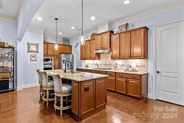 kitchen with a kitchen island with sink, sink, hanging light fixtures, appliances with stainless steel finishes, and dark hardwood / wood-style flooring