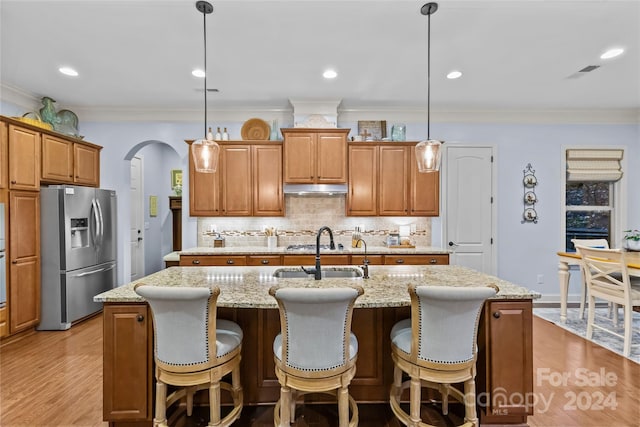 kitchen with stainless steel fridge, a kitchen island with sink, and pendant lighting