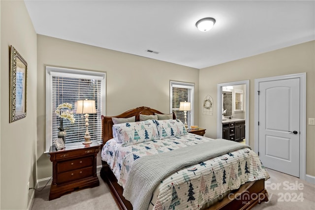 bedroom with ensuite bathroom and light colored carpet