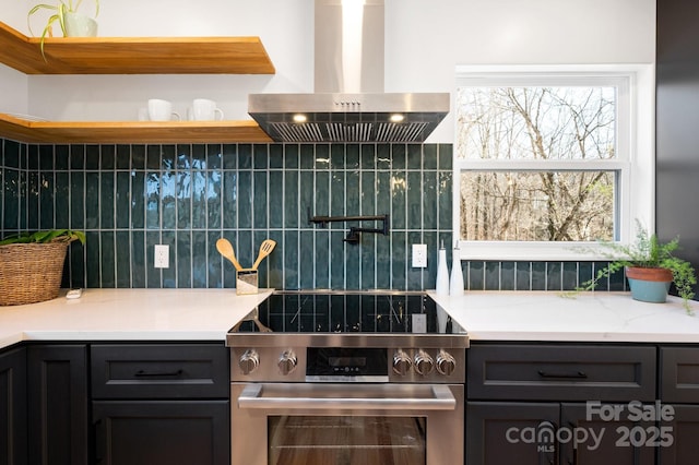 kitchen with decorative backsplash, light stone countertops, wall chimney range hood, and high end stainless steel range