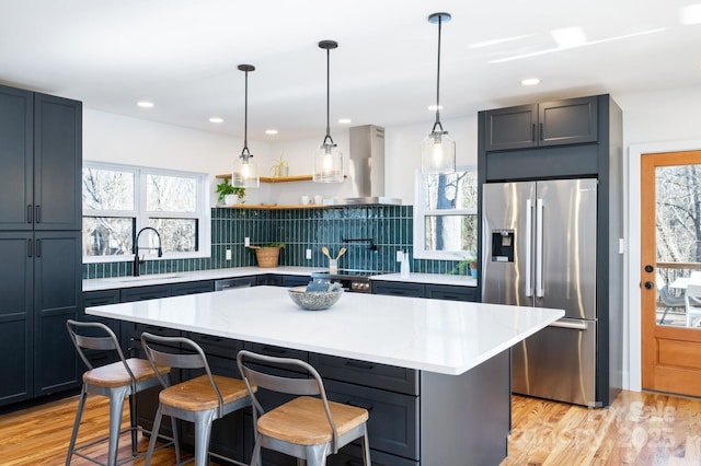 kitchen with decorative backsplash, appliances with stainless steel finishes, a kitchen bar, wall chimney range hood, and a kitchen island