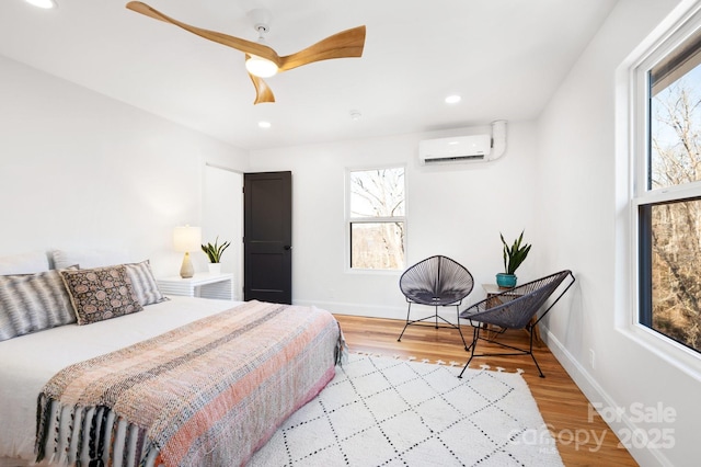 bedroom featuring a wall mounted AC, light hardwood / wood-style floors, and ceiling fan