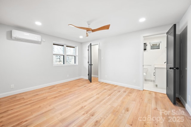 unfurnished bedroom featuring a wall unit AC, connected bathroom, ceiling fan, and light hardwood / wood-style flooring