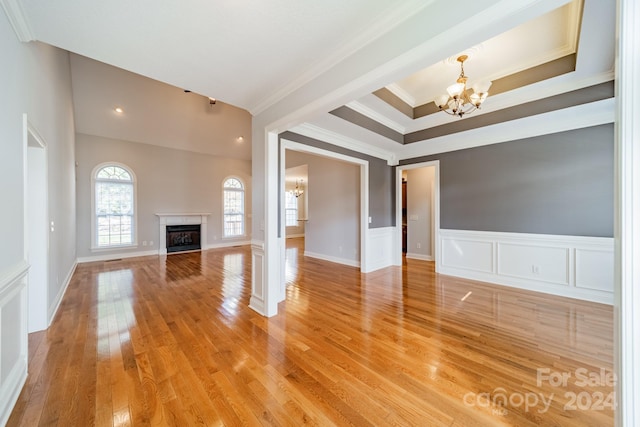 unfurnished living room featuring a high end fireplace, ornamental molding, a tray ceiling, hardwood / wood-style flooring, and a notable chandelier