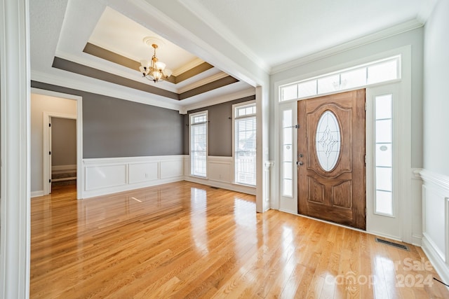 foyer with a tray ceiling, light hardwood / wood-style flooring, a notable chandelier, and ornamental molding