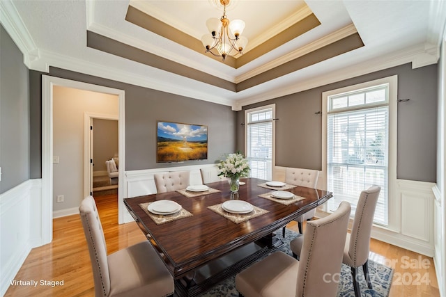 dining space with a notable chandelier, a raised ceiling, light wood-type flooring, and ornamental molding