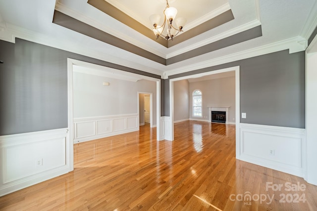 unfurnished living room with an inviting chandelier, crown molding, a tray ceiling, a fireplace, and hardwood / wood-style flooring