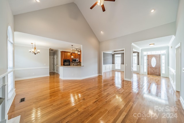 unfurnished living room with high vaulted ceiling, ceiling fan with notable chandelier, and light wood-type flooring