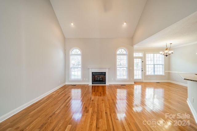 unfurnished living room with high vaulted ceiling, light hardwood / wood-style flooring, plenty of natural light, and a notable chandelier