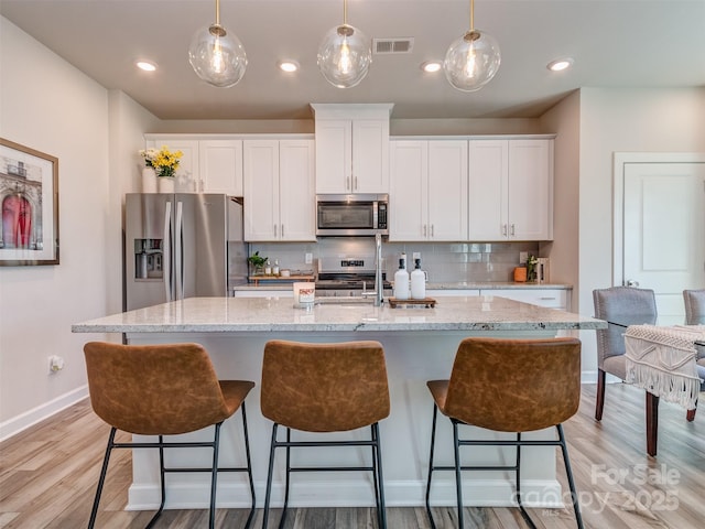 kitchen featuring appliances with stainless steel finishes, light wood-type flooring, tasteful backsplash, a kitchen island with sink, and white cabinets