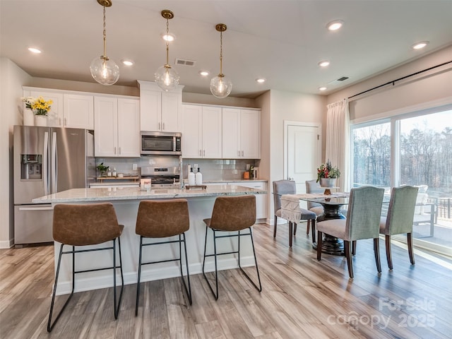 kitchen with light stone countertops, stainless steel appliances, light hardwood / wood-style floors, a center island with sink, and white cabinets