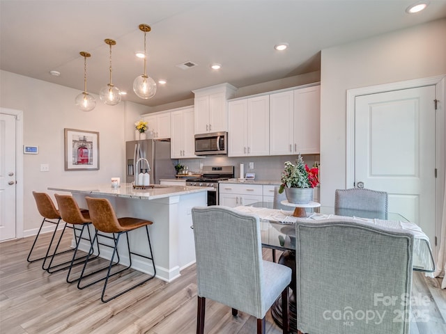 kitchen featuring backsplash, stainless steel appliances, pendant lighting, white cabinets, and an island with sink