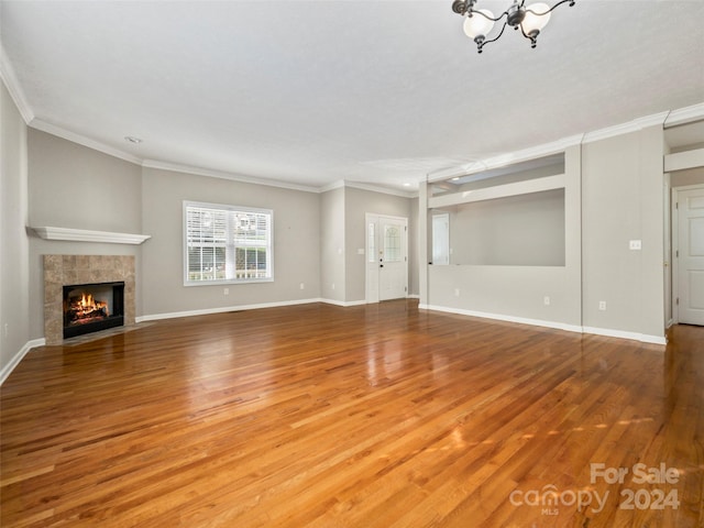 unfurnished living room featuring a tile fireplace, hardwood / wood-style floors, a chandelier, and crown molding