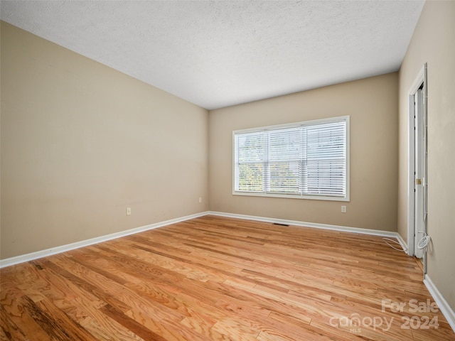 empty room with a textured ceiling and light hardwood / wood-style flooring