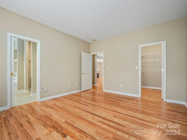 unfurnished bedroom with light hardwood / wood-style floors, a spacious closet, a textured ceiling, and a closet