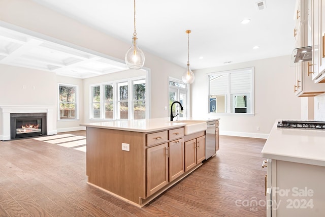 kitchen with coffered ceiling, stainless steel appliances, sink, a center island with sink, and light hardwood / wood-style floors