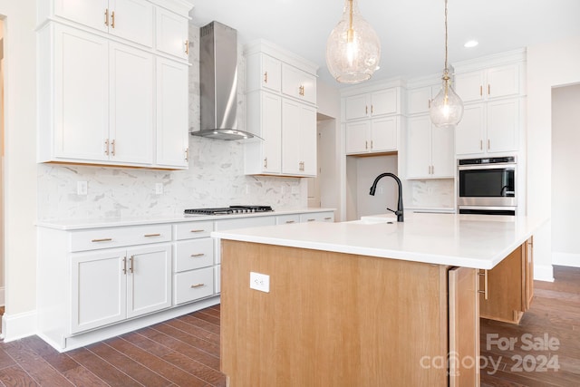 kitchen with white cabinetry, sink, wall chimney exhaust hood, dark wood-type flooring, and a kitchen island with sink