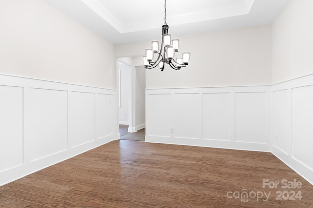 unfurnished dining area with a raised ceiling, dark wood-type flooring, and a notable chandelier