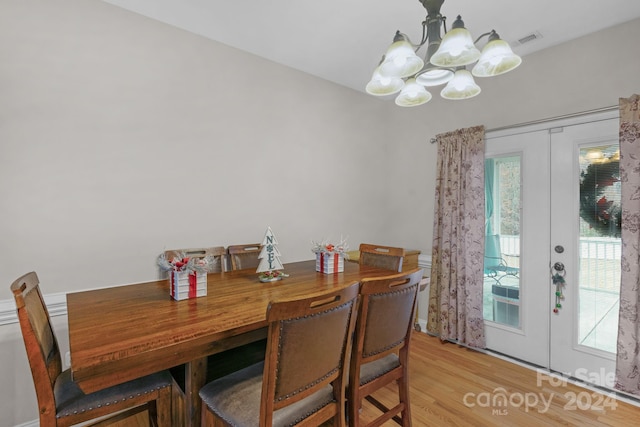 dining area with french doors, light wood-type flooring, and an inviting chandelier