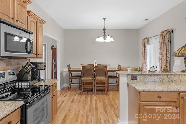 kitchen with decorative light fixtures, light hardwood / wood-style flooring, appliances with stainless steel finishes, a notable chandelier, and light stone counters