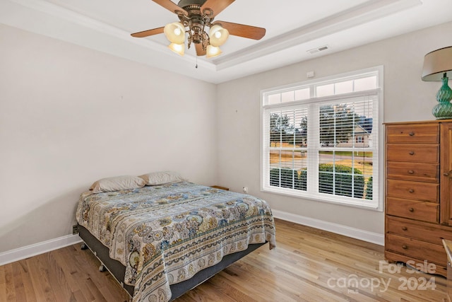 bedroom featuring a raised ceiling, ceiling fan, and light wood-type flooring