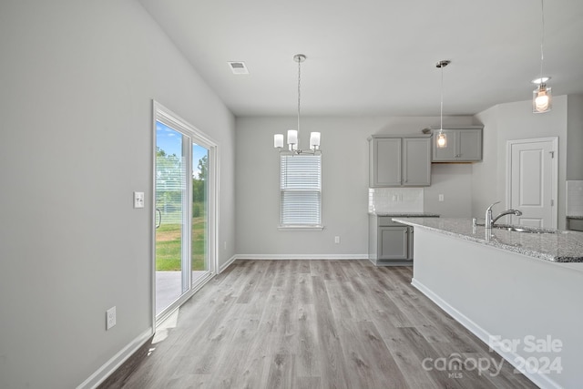 kitchen featuring gray cabinetry, sink, light stone counters, light hardwood / wood-style flooring, and decorative light fixtures