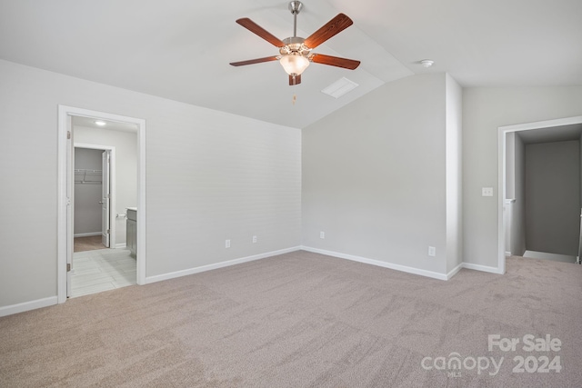 unfurnished bedroom featuring a spacious closet, light colored carpet, vaulted ceiling, and ceiling fan