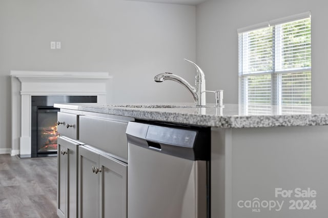 kitchen featuring light stone counters, stainless steel dishwasher, and light hardwood / wood-style floors