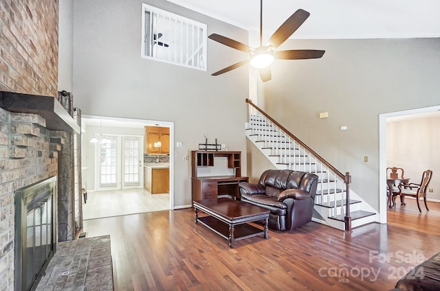 living room with a fireplace, wood-type flooring, a towering ceiling, and ceiling fan