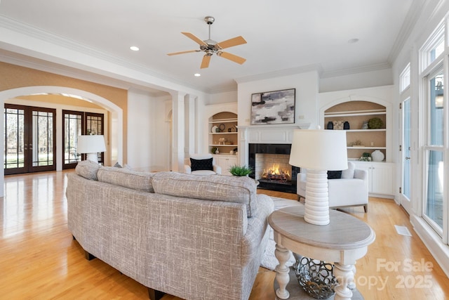 living room with light hardwood / wood-style flooring, built in shelves, plenty of natural light, and ornamental molding