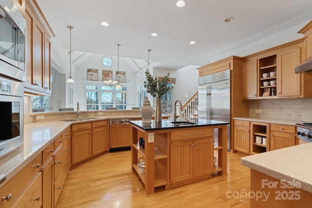 kitchen with hanging light fixtures, a center island with sink, sink, and built in appliances