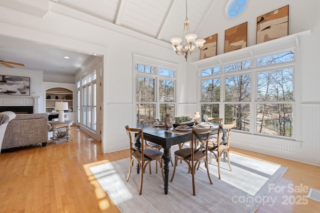 dining area with beam ceiling, light hardwood / wood-style flooring, built in features, and ceiling fan with notable chandelier