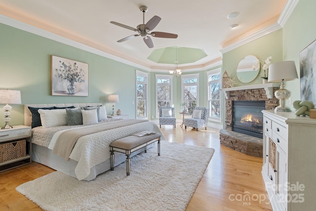 bedroom with a stone fireplace, ceiling fan with notable chandelier, ornamental molding, a raised ceiling, and light hardwood / wood-style flooring