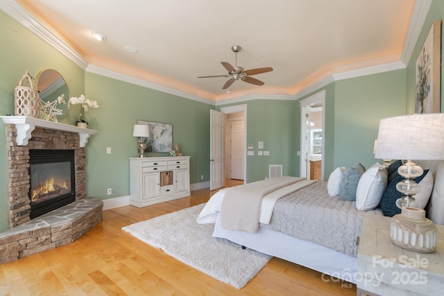 bedroom featuring ornamental molding, light wood-type flooring, ceiling fan, and a fireplace