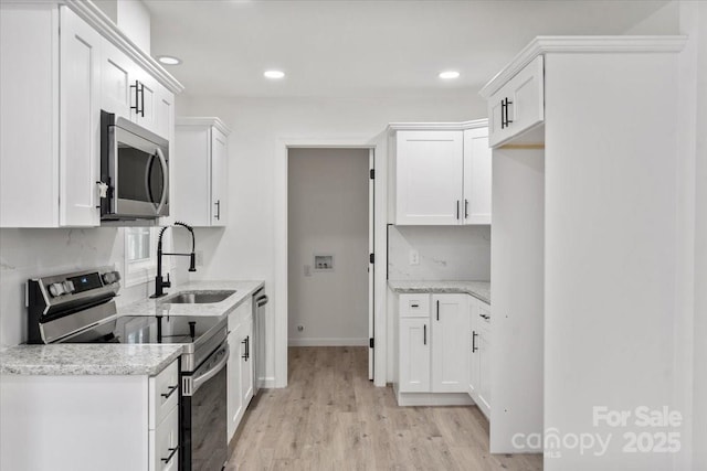 kitchen with sink, white cabinetry, light hardwood / wood-style flooring, appliances with stainless steel finishes, and light stone countertops