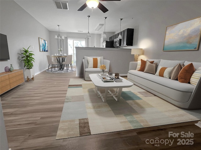 living area with ceiling fan with notable chandelier, light wood finished floors, visible vents, and baseboards