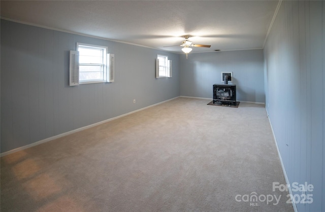 basement with ceiling fan, light colored carpet, a wood stove, and ornamental molding