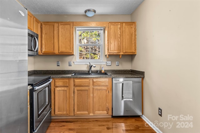 kitchen featuring appliances with stainless steel finishes, light wood-type flooring, a textured ceiling, and sink