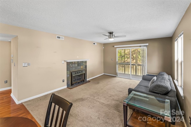 living room featuring a tiled fireplace, ceiling fan, wood-type flooring, and a textured ceiling