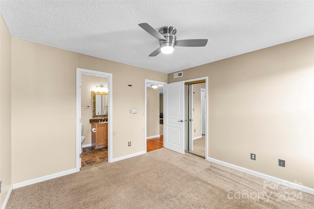 unfurnished bedroom with ensuite bathroom, ceiling fan, light colored carpet, and a textured ceiling