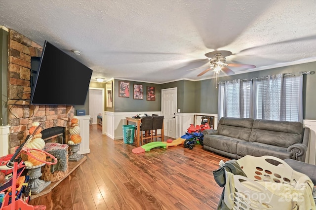 living room featuring a textured ceiling, ceiling fan, crown molding, hardwood / wood-style flooring, and a fireplace