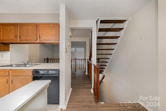 kitchen featuring hardwood / wood-style floors, sink, black dishwasher, and a textured ceiling