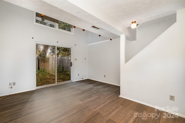 spare room with dark hardwood / wood-style flooring, a towering ceiling, and a textured ceiling