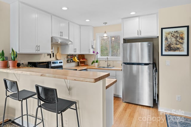 kitchen with a kitchen breakfast bar, stainless steel refrigerator, kitchen peninsula, and white cabinets