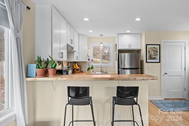 kitchen featuring stainless steel fridge, a kitchen breakfast bar, white cabinets, and hanging light fixtures