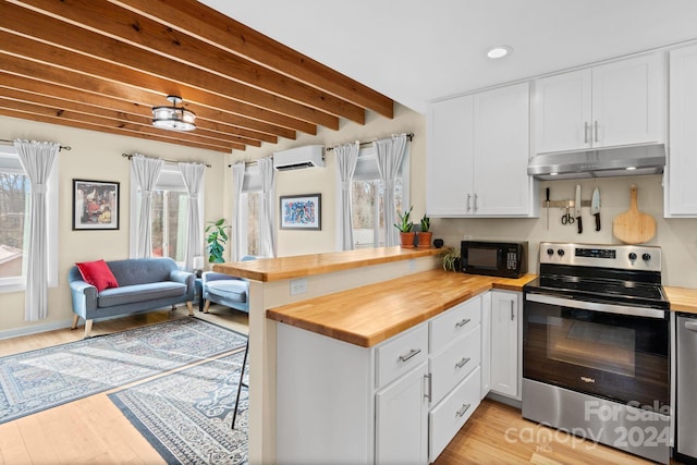 kitchen with wooden counters, stainless steel range with electric stovetop, a wall unit AC, beam ceiling, and white cabinets