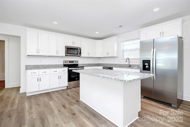 kitchen featuring white cabinetry, light stone counters, stainless steel appliances, and a kitchen island