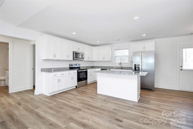 kitchen featuring stainless steel appliances, a center island, light stone countertops, and white cabinets